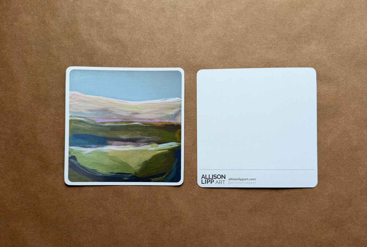 A square art print showing an abstract landscape painting with green hills, blue sky, and soft pink and purple tones, displayed next to its white backing card on a brown kraft paper background. The backing card features the text 'ALLISON CLIPPART' and 'allisonclipart.