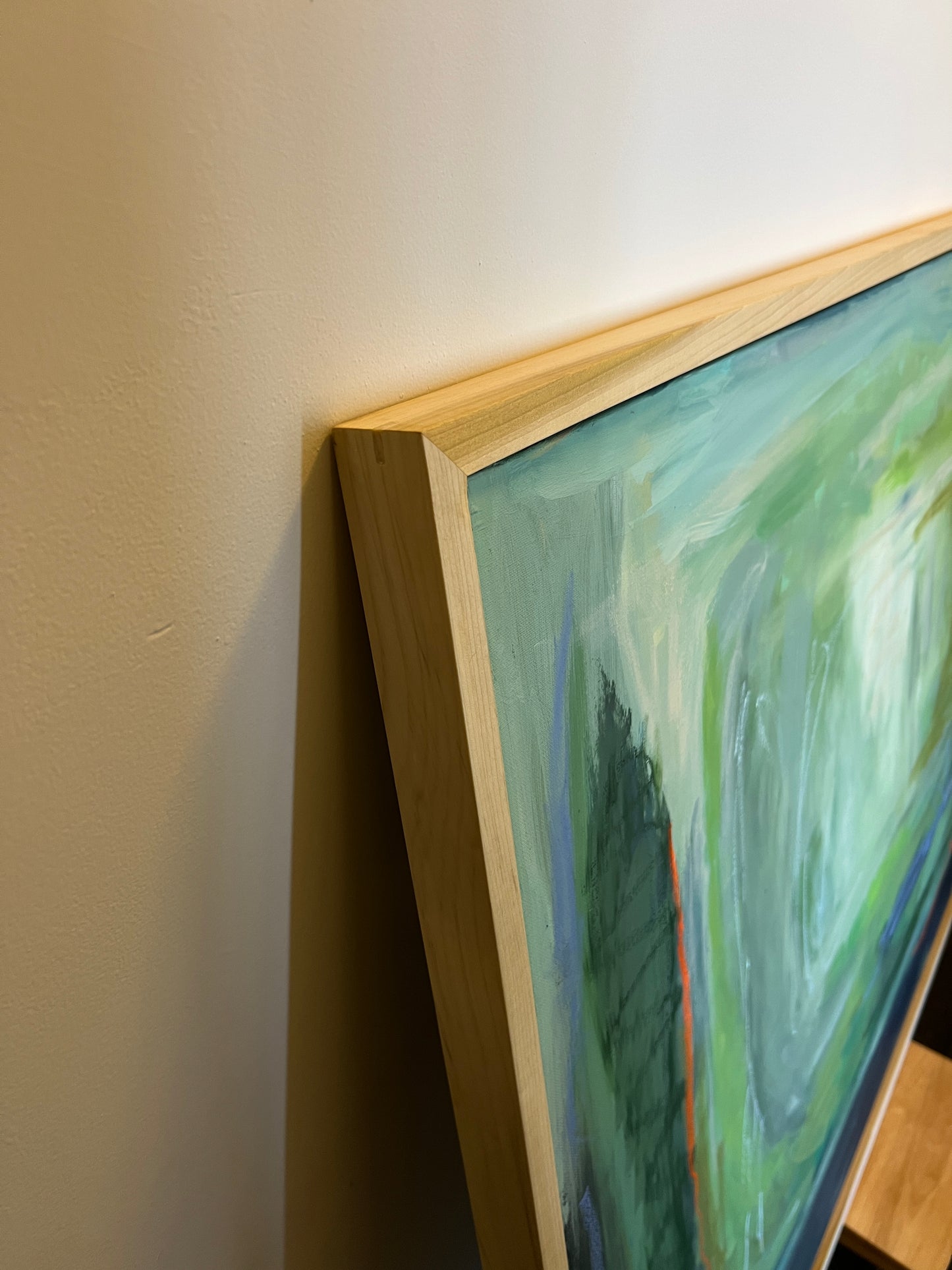 Close-up of a framed abstract painting with a wooden frame on a light surface.