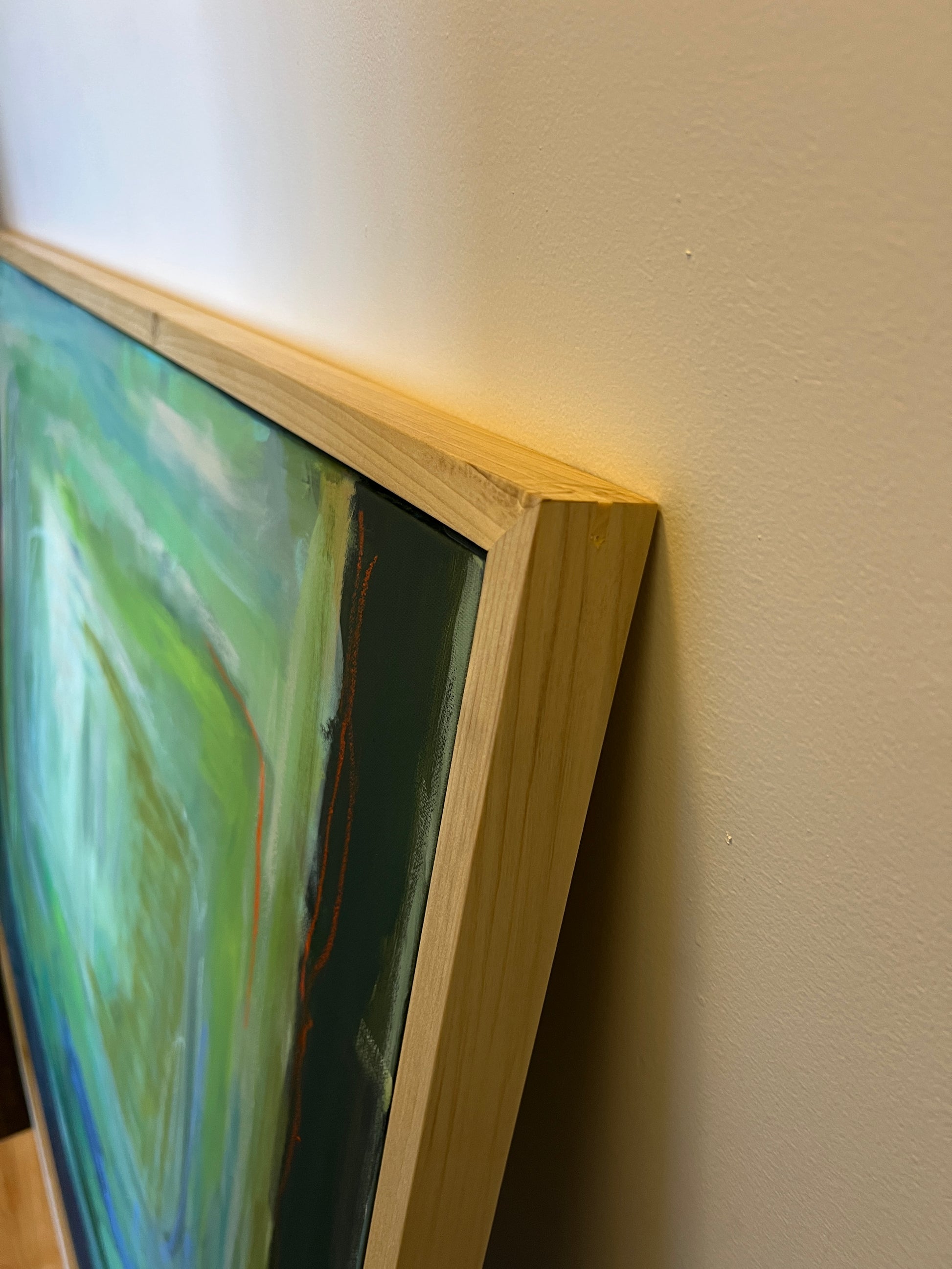 Partial view of a painting with a wooden frame on a white wall.