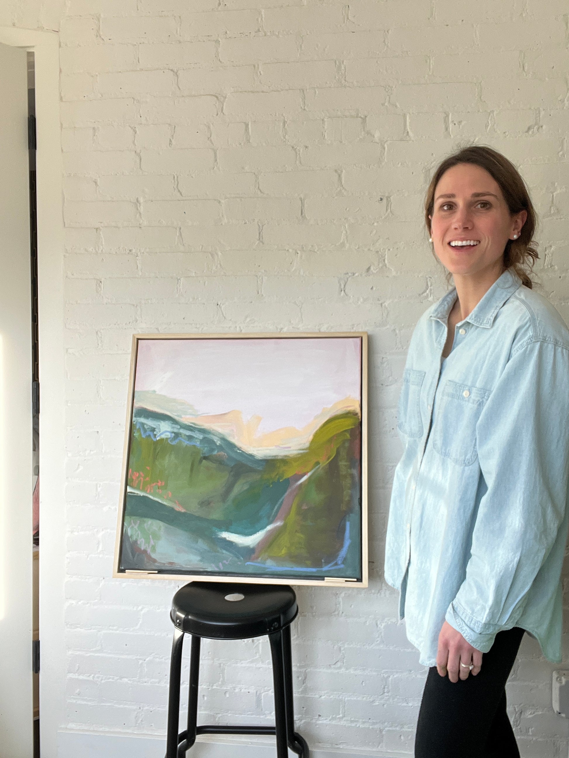 Person standing next to a framed abstract painting on a white brick wall.