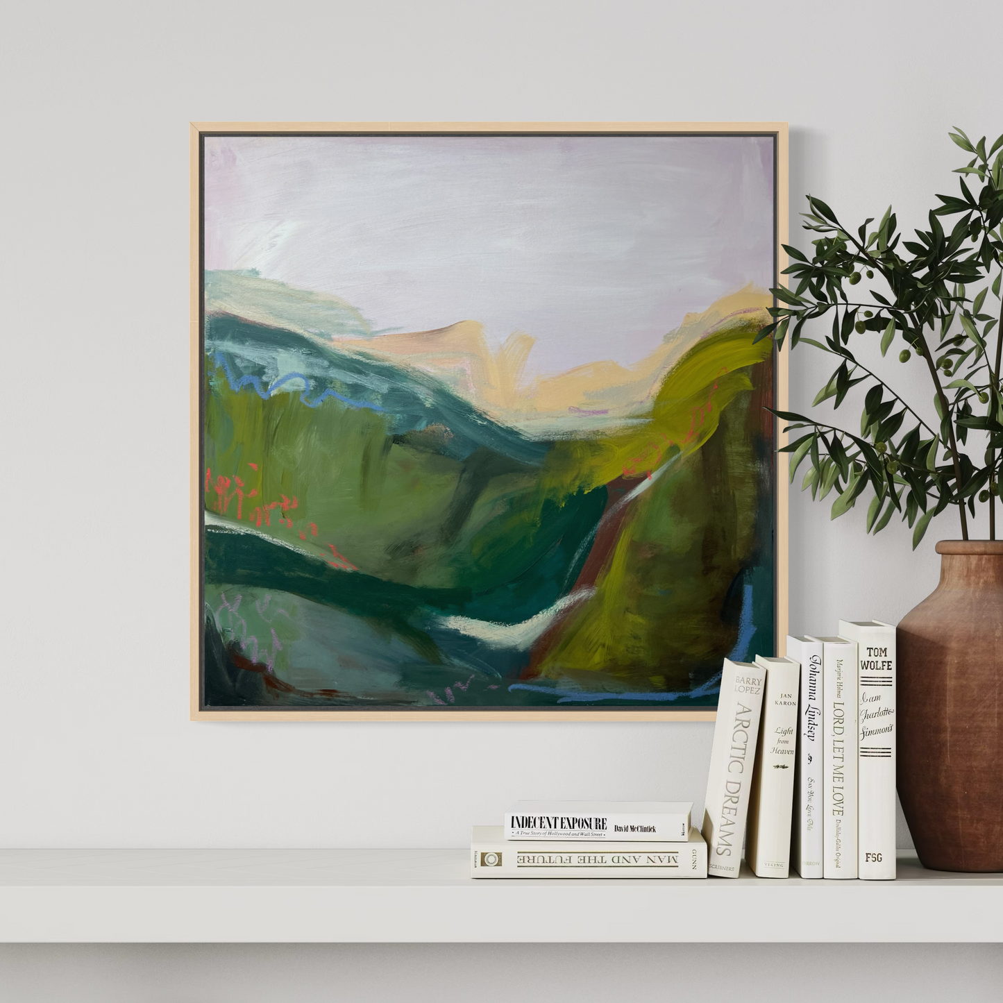 Framed abstract landscape painting on a wall with books and a vase below.